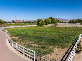 Discover this expansive property featuring a charming white vinyl fence that encloses a lush green pasture, perfect for equestrian activities or simply enjoying the open space.