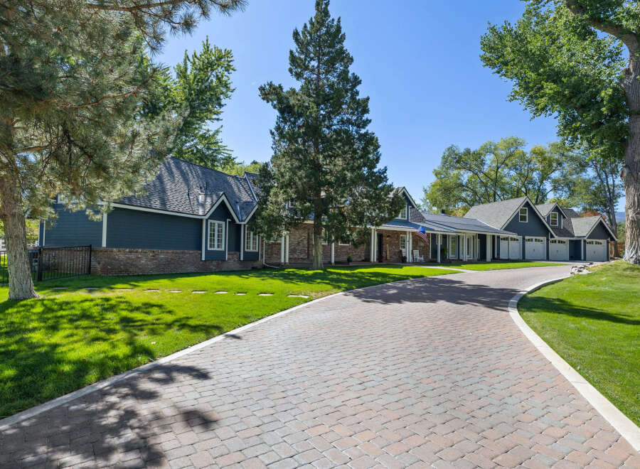 This stunning property features a long, winding paver driveway leading to a charming home with a dark blue exterior and brick accents.