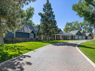 This stunning property features a long, winding paver driveway leading to a charming home with a dark blue exterior and brick accents.