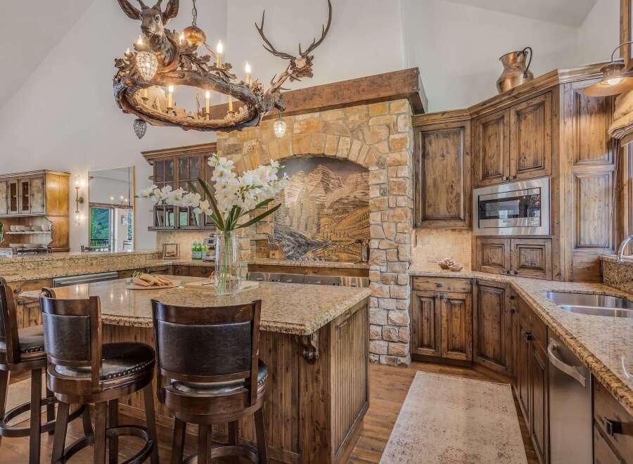 Experience rustic luxury in this stunning kitchen featuring a grand stone fireplace and a unique antler chandelier.