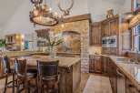 Experience rustic luxury in this stunning kitchen featuring a grand stone fireplace and a unique antler chandelier.