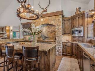 Experience rustic luxury in this stunning kitchen featuring a grand stone fireplace and a unique antler chandelier.