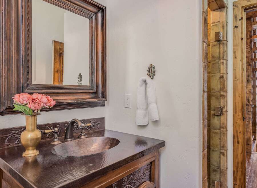 This rustic bathroom features a hammered copper sink and countertop, complemented by a dark wood vanity with intricate carved details.