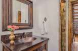 This rustic bathroom features a hammered copper sink and countertop, complemented by a dark wood vanity with intricate carved details.