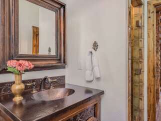 This rustic bathroom features a hammered copper sink and countertop, complemented by a dark wood vanity with intricate carved details.