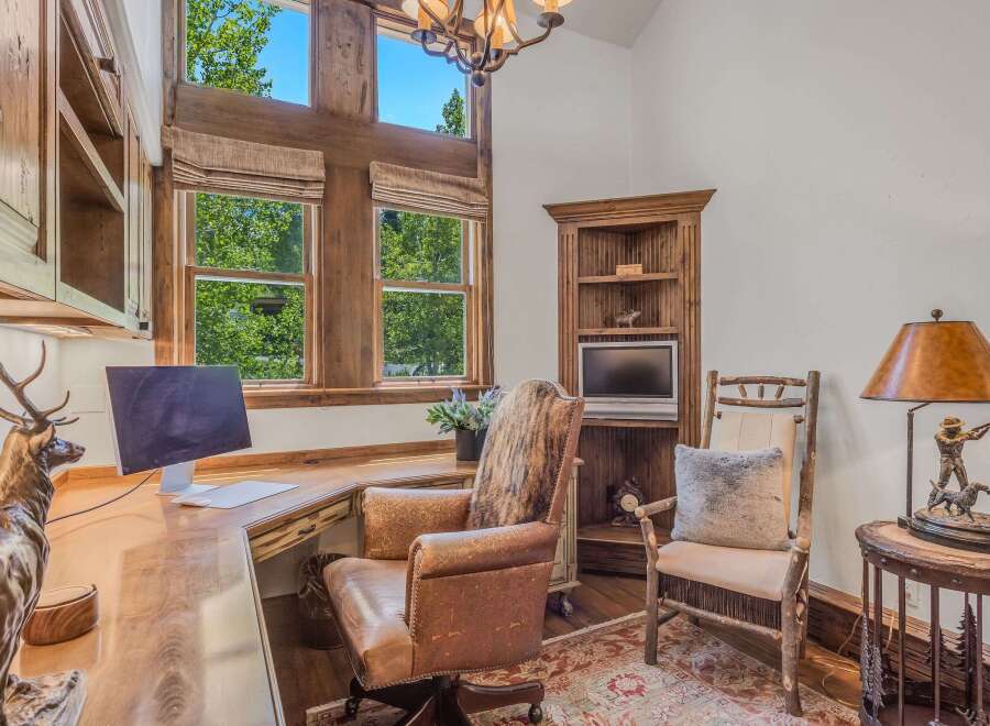 Discover a rustic home office featuring a large wooden desk with a computer, complemented by a comfortable leather executive chair and a unique animal hide accent.