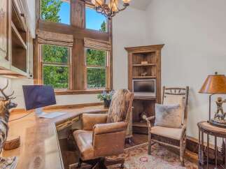 Discover a rustic home office featuring a large wooden desk with a computer, complemented by a comfortable leather executive chair and a unique animal hide accent.