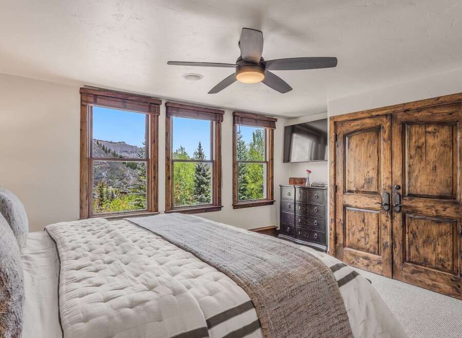 Experience breathtaking mountain views from this luxurious bedroom, featuring three large windows that frame the stunning landscape.