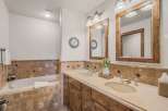 This luxurious bathroom features a deep soaking tub and a spacious double vanity with rustic wooden cabinetry.
