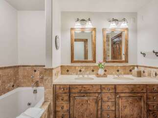 Experience luxury in this stunning bathroom featuring a deep soaking tub and a spacious double vanity with rustic wooden cabinetry.