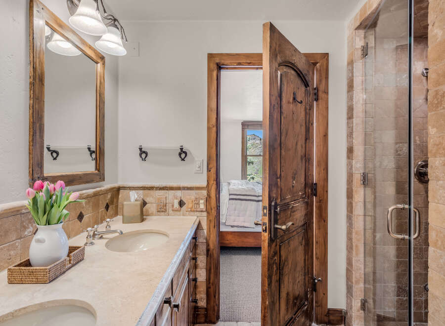 Experience rustic charm in this bathroom featuring a double vanity with a travertine countertop and a wooden-framed mirror.