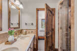 Experience rustic charm in this bathroom featuring a double vanity with a travertine countertop and a wooden-framed mirror.