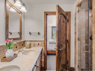 Experience rustic charm in this bathroom featuring a double vanity with a travertine countertop and a wooden-framed mirror.