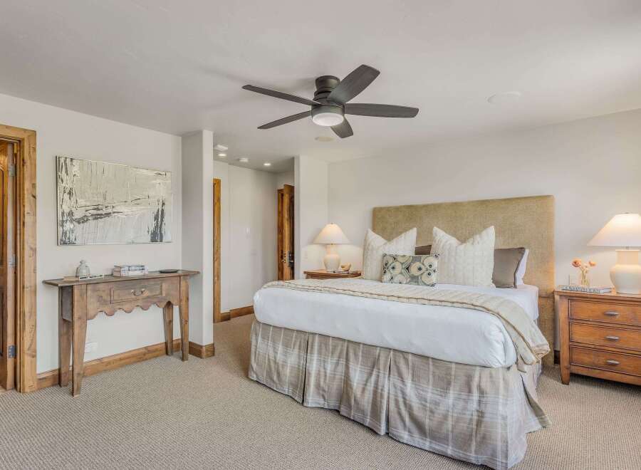 Experience ultimate comfort in this master suite, featuring a plush king-sized bed with a textured headboard and a charming plaid bed skirt.