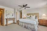 Experience ultimate comfort in this master suite, featuring a plush king-sized bed with a textured headboard and a charming plaid bed skirt.