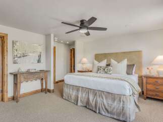 Experience ultimate comfort in this master suite, featuring a plush king-sized bed with a textured headboard and a charming plaid bed skirt.