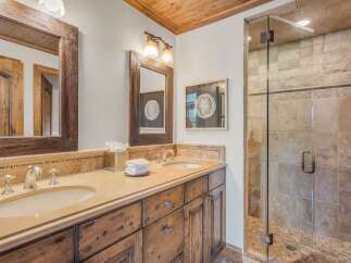 This luxurious bathroom features a spacious double vanity with a granite countertop and wooden cabinetry, complemented by elegant fixtures.