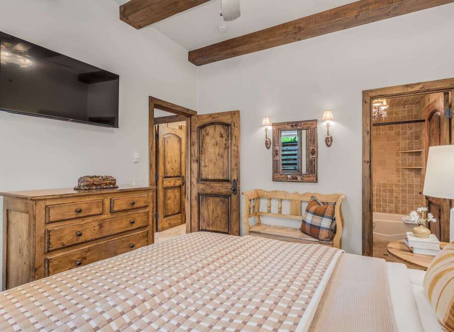 Experience rustic charm in this inviting bedroom featuring exposed wooden beams and a large flat-screen TV.