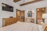 Experience rustic charm in this inviting bedroom featuring exposed wooden beams and a large flat-screen TV.