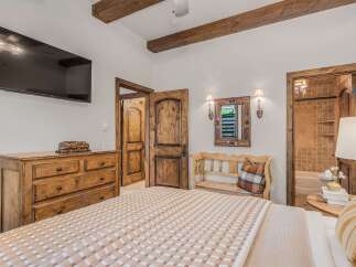 Experience rustic charm in this inviting bedroom featuring exposed wooden beams and a large flat-screen TV.