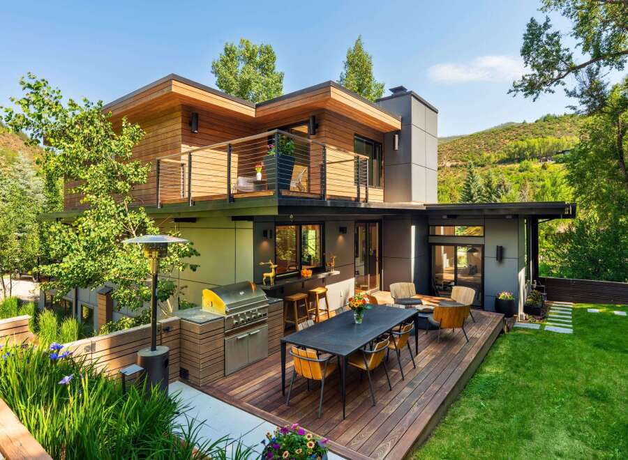 Experience luxurious outdoor living with this modern home featuring a spacious deck, built-in grill, and comfortable seating areas perfect for entertaining.