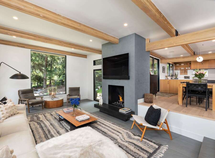 Experience modern living in this stunning open-concept space, featuring exposed wooden beams and a sleek, gray concrete fireplace as the centerpiece.