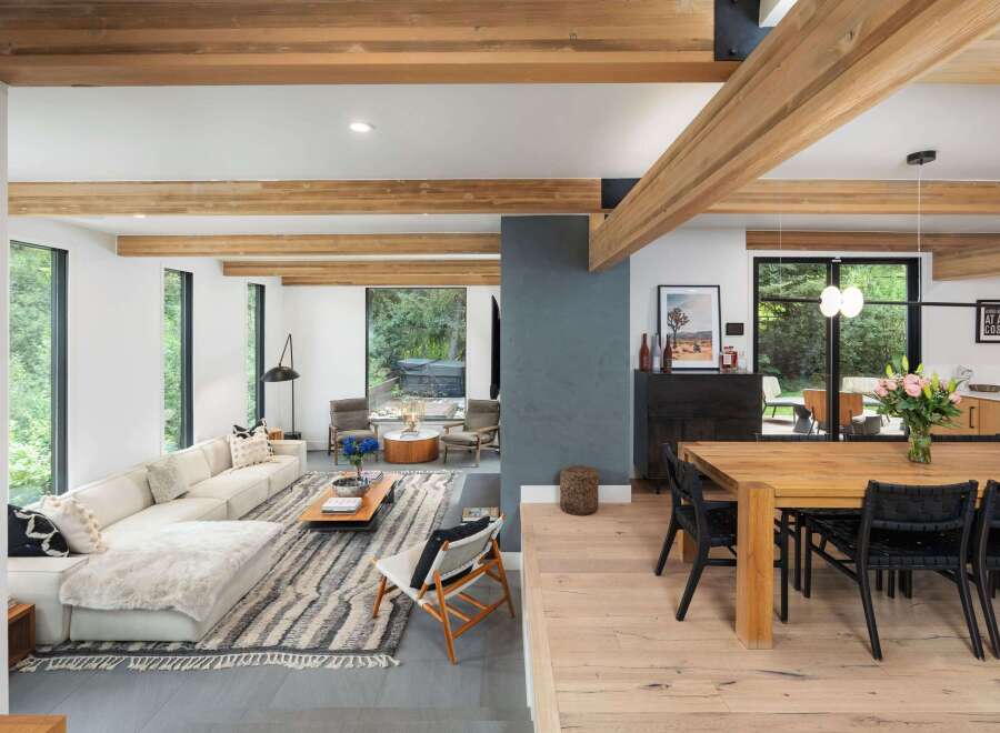 Experience modern living in this open-concept space featuring exposed wooden beams and large windows that flood the area with natural light.