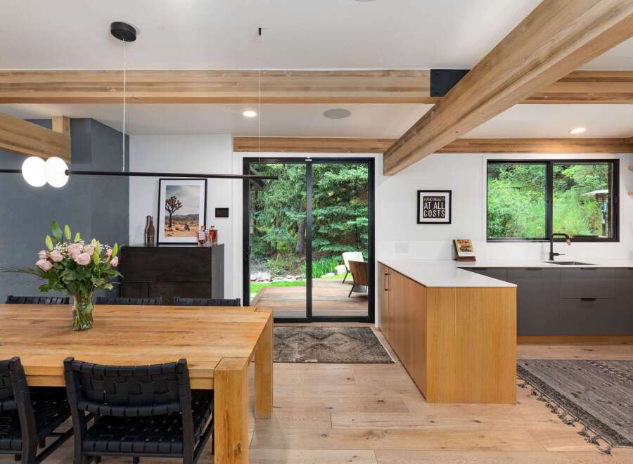 Experience modern living in this stunning open-concept dining and kitchen area, featuring exposed wooden beams and a sleek, minimalist design.