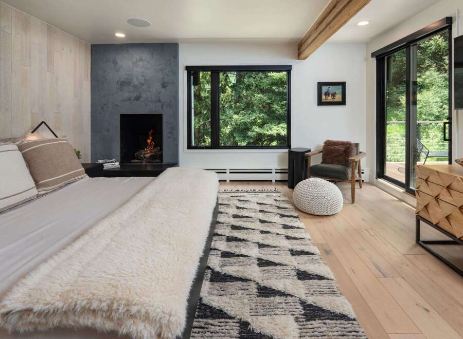 Experience luxury mountain living in this stunning bedroom featuring a modern fireplace and expansive windows showcasing breathtaking forest views.