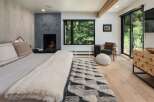 Experience luxury mountain living in this stunning bedroom featuring a modern fireplace and expansive windows showcasing breathtaking forest views.
