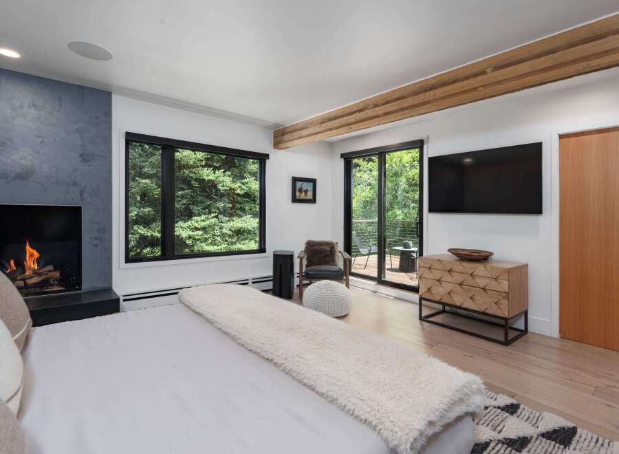 Experience luxury living in this stunning bedroom featuring a modern fireplace and expansive windows offering serene forest views.