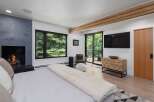 Experience luxury living in this stunning bedroom featuring a modern fireplace and expansive windows offering serene forest views.