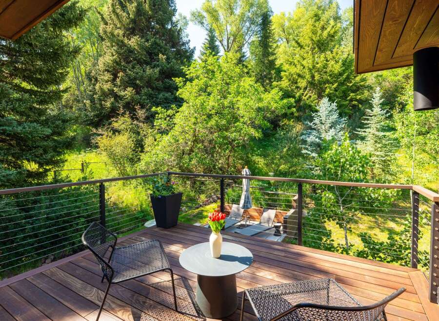 Enjoy serene outdoor living on this spacious wooden deck, surrounded by lush greenery and mature trees.