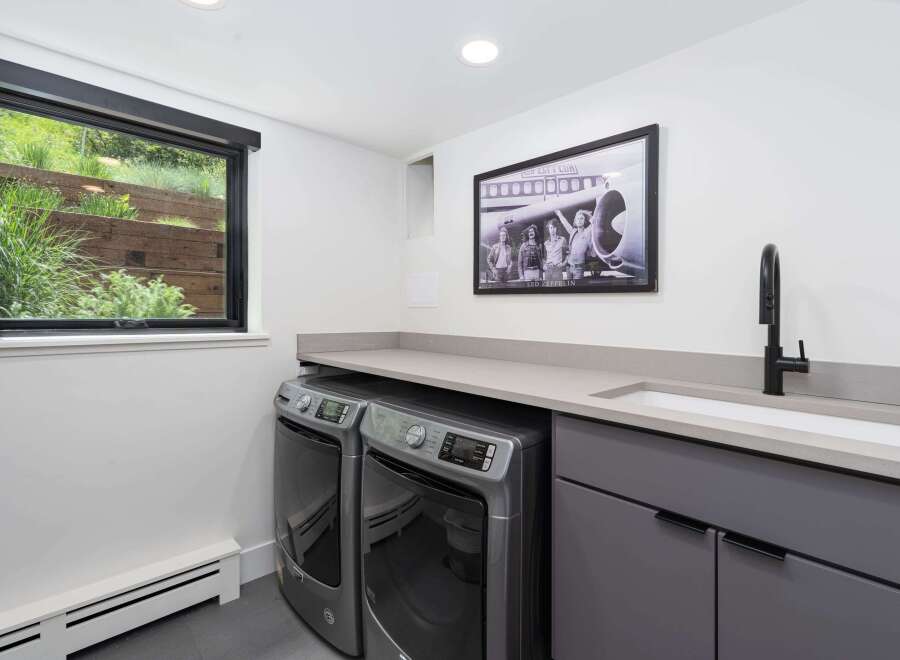 This modern laundry room features a sleek grey cabinetry set with integrated sink and a black faucet, complemented by a light grey countertop.