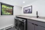 This modern laundry room features a sleek grey cabinetry set with integrated sink and a black faucet, complemented by a light grey countertop.
