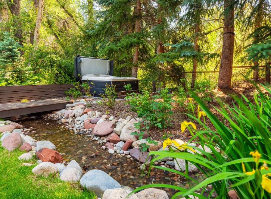 Escape to your private oasis with this stunning backyard featuring a luxurious hot tub nestled amongst lush greenery.