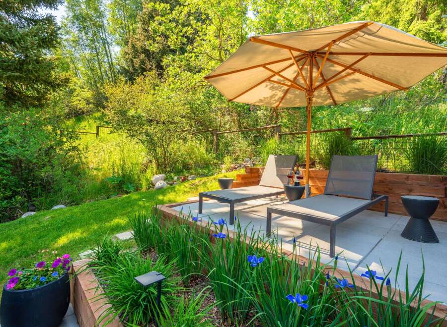 Relax and unwind in this serene outdoor oasis, featuring comfortable lounge chairs under a large umbrella, perfect for enjoying the lush greenery.