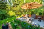 Relax and unwind in this serene outdoor oasis, featuring comfortable lounge chairs under a large umbrella, perfect for enjoying the lush greenery.