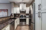 This modern kitchen boasts sleek stainless steel appliances, including a refrigerator, oven, and dishwasher, complemented by elegant white cabinetry and granite countertops.