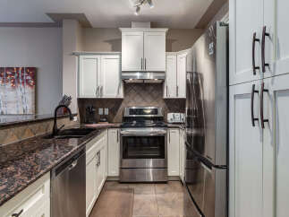 This modern kitchen boasts sleek stainless steel appliances, including a refrigerator, oven, and dishwasher, complemented by elegant white cabinetry and granite countertops.