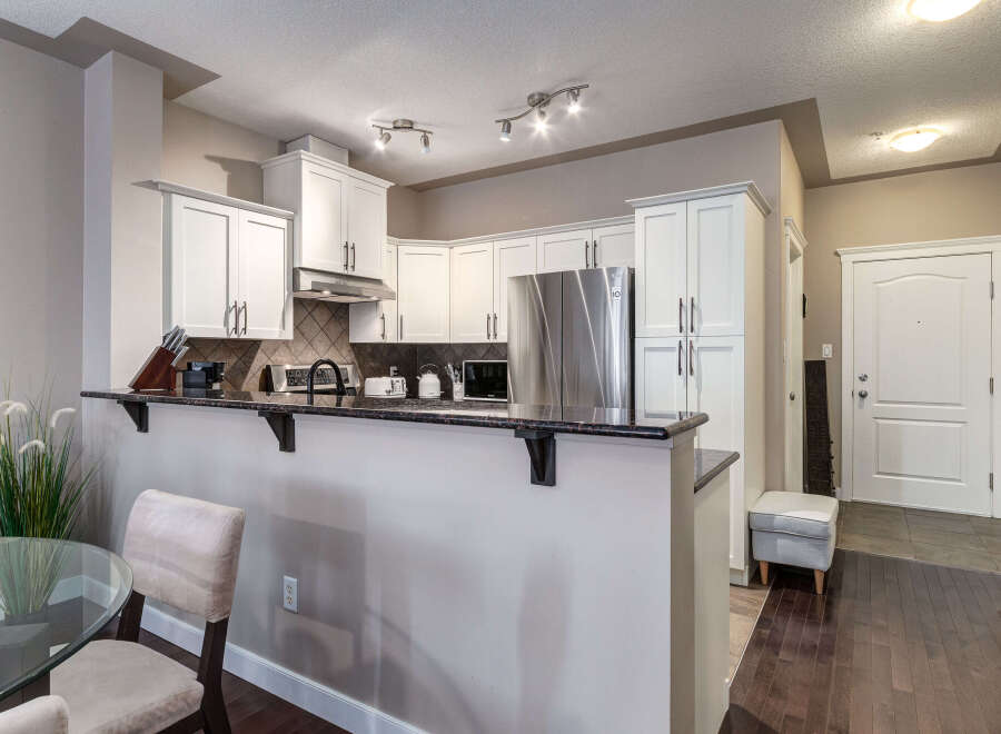 Discover this stunning kitchen featuring sleek white cabinetry, a granite countertop, and a stainless steel refrigerator.
