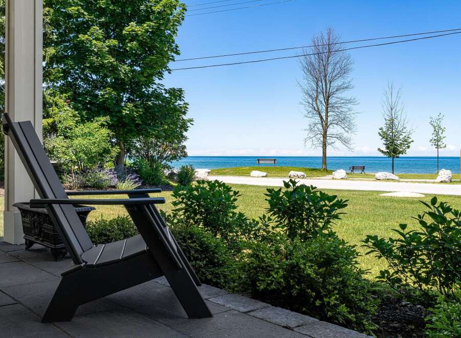 Enjoy serene lakefront living from this charming property, featuring a comfortable Adirondack chair on the porch overlooking a lush green lawn and the sparkling blue water.