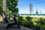 Enjoy serene lakefront living from this charming property, featuring a comfortable Adirondack chair on the porch overlooking a lush green lawn and the sparkling blue water.