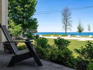 Enjoy serene lakefront living from this charming property, featuring a comfortable Adirondack chair on the porch overlooking a lush green lawn and the sparkling blue water.