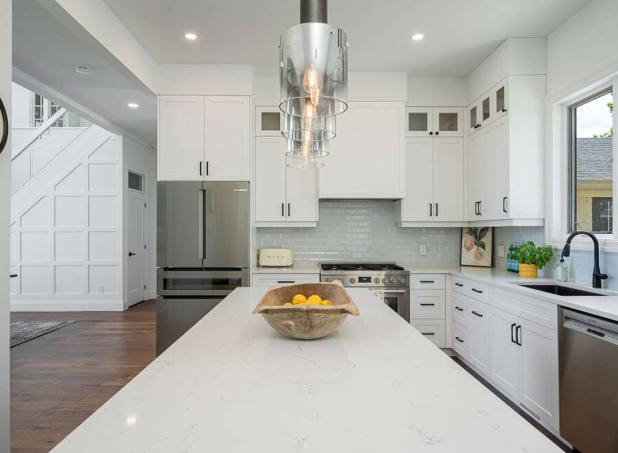 Experience modern luxury in this stunning kitchen, featuring sleek white cabinetry, a spacious quartz island with a decorative bowl of lemons, and a professional-grade stainless steel range.