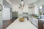 Experience modern luxury in this stunning kitchen, featuring sleek white cabinetry, a spacious quartz island with a decorative bowl of lemons, and a professional-grade stainless steel range.