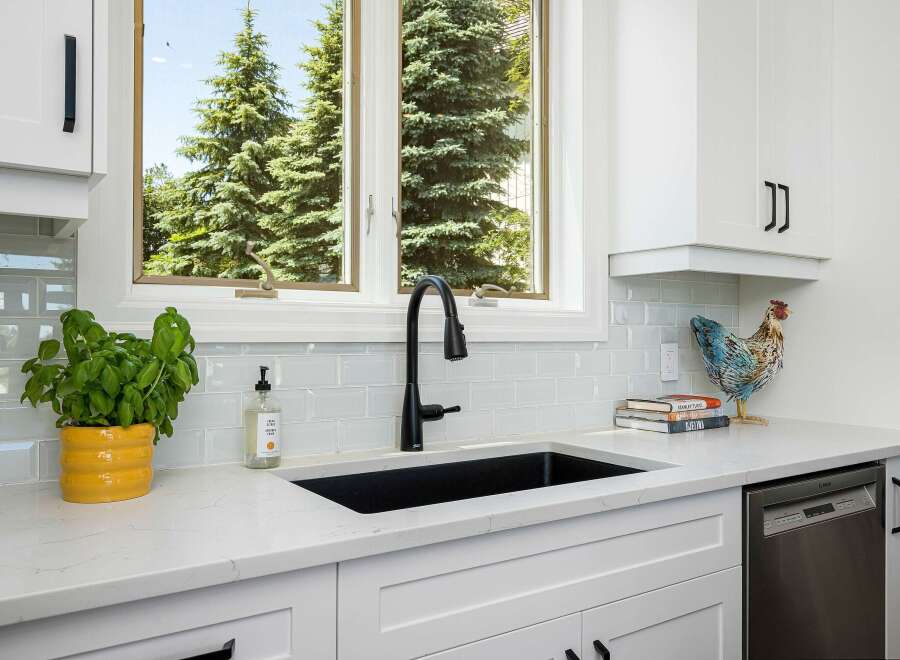 This modern kitchen features a sleek black sink and faucet, complemented by a light blue subway tile backsplash.