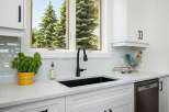 This modern kitchen features a sleek black sink and faucet, complemented by a light blue subway tile backsplash.