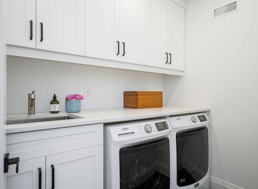 This laundry room features a sleek white cabinetry setup with modern black hardware, providing ample storage above a spacious countertop.