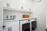 This laundry room features a sleek white cabinetry setup with modern black hardware, providing ample storage above a spacious countertop.
